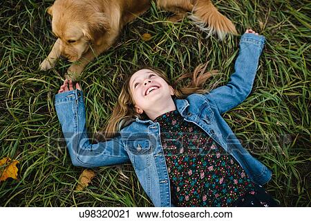 Stock Image - Young girl lying on grass looking up at her Golden Retriever. Fotosearch