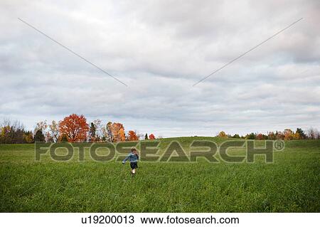 Stock Image - Young girl running in open field, Lakefield, Ontario, Canada. Fotosearch