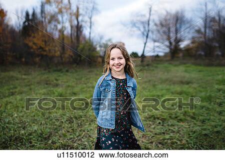 Stock Image - Young girl smiling in field in denim jacket, Lakefield, Ontario, Canada. Fotosearch