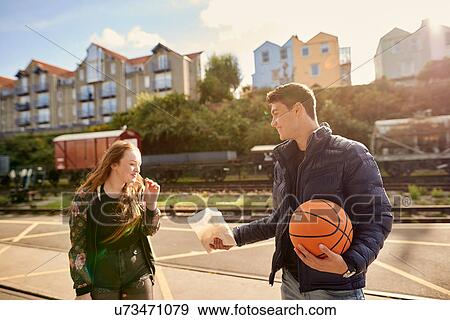 Stock Photo - Young man sharing bag of chips with friend, young man holding basketball, Bristol, UK. Fotosearch