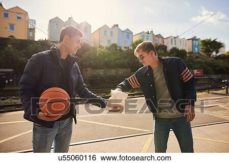 Stock Photograph - Young man sharing bag of chips with friend, young man holding basketball, Bristol, UK. Fotosearch