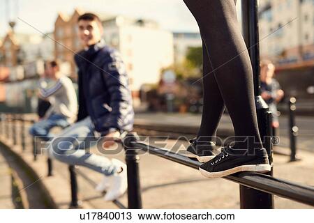 Young man sitting on railing, young girl walking along railing next to him, Bristol, UK View Large Photo Image Stock Image - Young man sitting on railing, young girl walking along railing next to him, Bristol, UK. Fotosearch