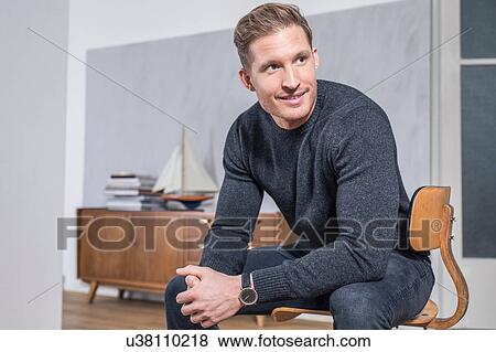 Young man sitting on vintage office chair in living room looking over his shoulder View Large Photo Image Stock Photo - Young man sitting on vintage office chair in living room looking over his shoulder. Fotosearch