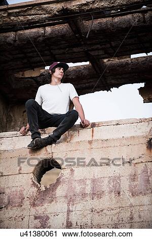 Young man sitting on wall at ruined mine View Large Photo Image Stock Image - Young man sitting on wall at ruined mine. Fotosearch