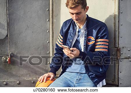 Young man sitting outdoors, using smartphone, holding basketball, Bristol, UK View Large Photo Image Stock Image - Young man sitting outdoors, using smartphone, holding basketball, Bristol, UK. Fotosearch