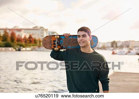Young man walking beside river, carrying skateboard, Bristol, UK View Large Photo Image Stock Photo - Young man walking beside river, carrying skateboard, Bristol, UK. Fotosearch