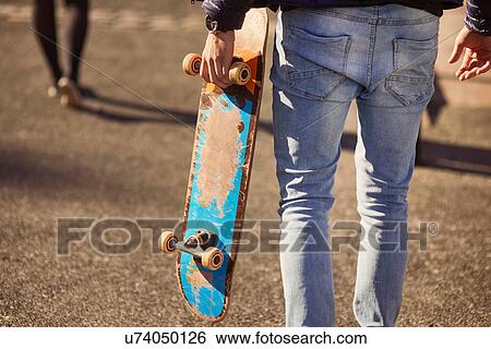 Young man walking outdoors, carrying skateboard, rear view, low section, Bristol, UK View Large Photo Image Stock Photograph - Young man walking outdoors, carrying skateboard, rear view, low section, Bristol, UK. Fotosearch