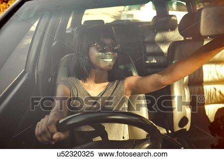 Stock Photography - Young woman adjusting rear view mirror in car, view through car window. Fotosearch