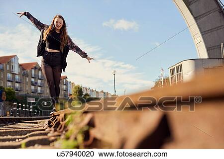 Stock Image - Young woman balancing on train track, low angle view, Bristol, UK. Fotosearch