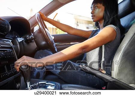Stock Image - Young woman driving car, low angle view. Fotosearch