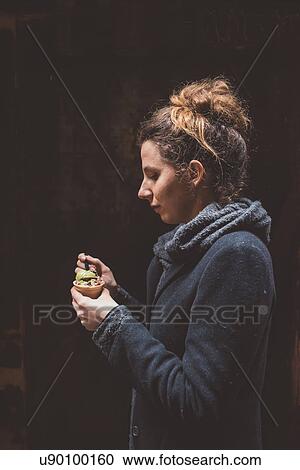 Stock Image - Young woman eating gelato in dark alley, Venice, Italy. Fotosearch