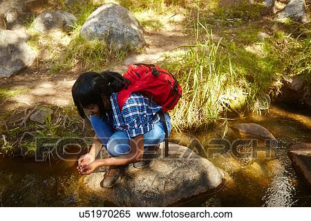 Stock Photography - Young woman, hiking, crouching on rock beside stream, Cape Town, South Africa. Fotosearch