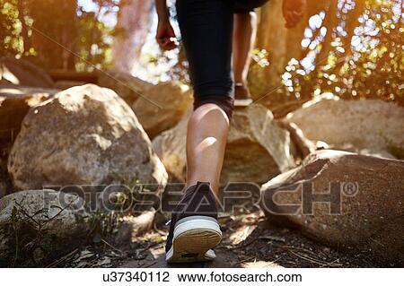 Stock Image - Young woman hiking through rural setting, rear view, low section. Fotosearch