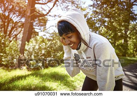 Stock Image - Young woman in rural setting, wearing hooded sweatshirt, smiling. Fotosearch