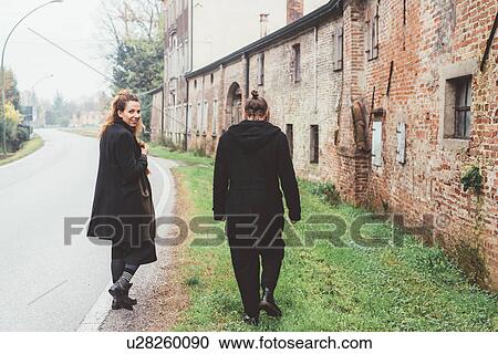 Stock Image - Young woman looking back while strolling with boyfriend on rural road. Fotosearch
