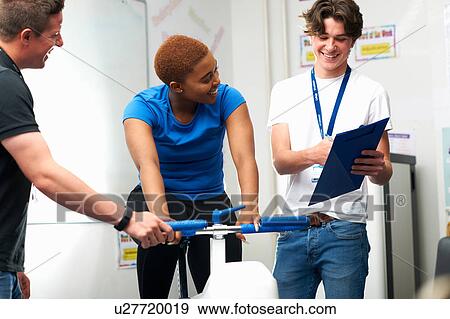Young woman on exercise bike, young man assessing fitness levels View Large Photo Image Stock Photo - Young woman on exercise bike, young man assessing fitness levels. Fotosearch