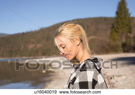 Stock Photo - Young woman on lakeside looking down, Bavarian Alps. Fotosearch