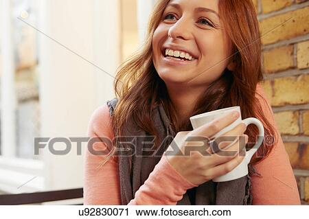 Young woman sitting outdoors, holding coffee cup, smiling View Large Photo Image Stock Image - Young woman sitting outdoors, holding coffee cup, smiling. Fotosearch