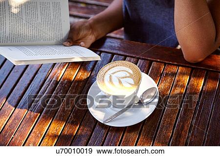 Young woman sitting outdoors, reading book, coffee in front of her, mid section View Large Photo Image Stock Photo - Young woman sitting outdoors, reading book, coffee in front of her, mid section. Fotosearch