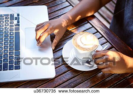Young woman sitting outdoors, using laptop, drinking coffee, mid section View Large Photo Image Stock Photography - Young woman sitting outdoors, using laptop, drinking coffee, mid section. Fotosearch