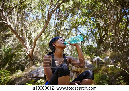 Young woman sitting outdoors, wearing sports clothing, drinking from water bottle View Large Photo Image Stock Image - Young woman sitting outdoors, wearing sports clothing, drinking from water bottle. Fotosearch