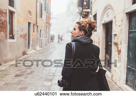 Young woman with camera looking over her shoulder on street, Venice, Italy View Large Photo Image Stock Image - Young woman with camera looking over her shoulder on street, Venice, Italy. Fotosearch