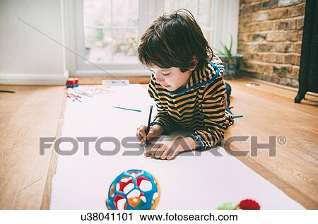 Stock Image - Boy lying on floor drawing on long paper. Fotosearch