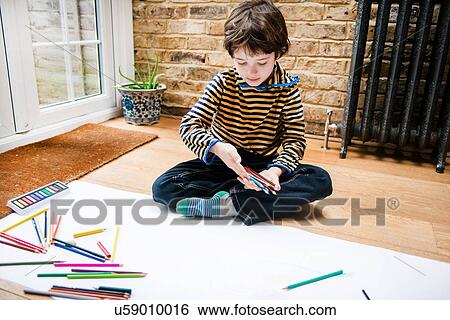 Stock Photograph - Boy sitting on floor drawing on long paper. Fotosearch