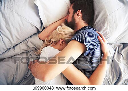 Stock Photo - Couple lying in bed together, sleeping, arms around each other. Fotosearch