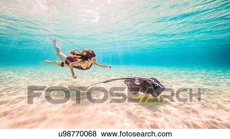Stock Photo - Female free diver swimming with stingray on seabed. Fotosearch