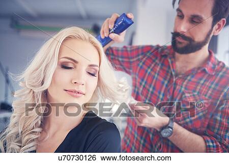 Stock Photograph - Male hairdresser putting hairspray on model for photo shoot. Fotosearch