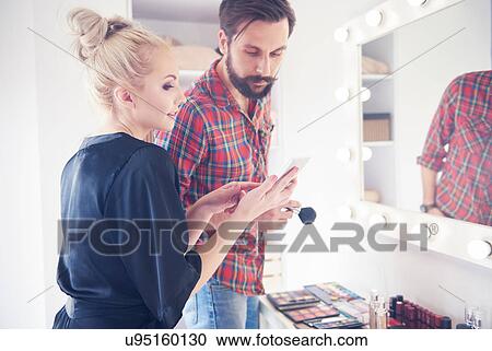 Stock Image - Male make up artist and model looking at smartphone before photo shoot. Fotosearch