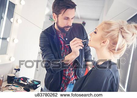 Stock Image - Male make up artist applying lipstick to model for photo shoot. Fotosearch