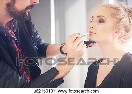 Stock Photo - Male make up artist applying lipstick to model for photo shoot. Fotosearch