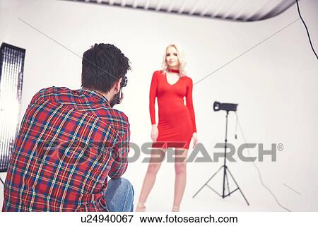 Stock Photo - Male photographer crouching to photograph female model on studio white background. Fotosearch