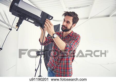 Stock Image - Male photographer preparing photo shoot lighting equipment in studio. Fotosearch