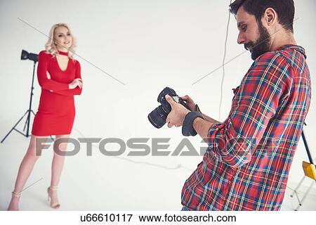 Stock Photo - Male photographer reviewing shoot of female model on studio white background. Fotosearch
