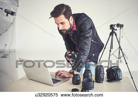 Stock Photography - Male photographer reviewing studio photo shoot on laptop. Fotosearch