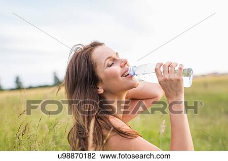 Mid adult woman drinking bottled water in field View Large Photo Image Stock Image - Mid adult woman drinking bottled water in field. Fotosearch