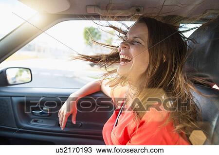 Stock Image - Mid adult woman with flyaway hair in front seat of car. Fotosearch