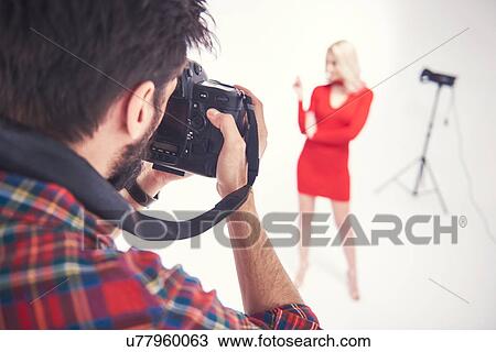 Stock Image - Over shoulder view of male photographer photographing female model on studio white background. Fotosearch