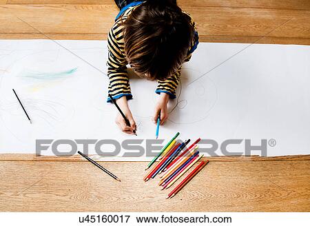 Stock Photo - Overhead view of boy lying on floor drawing on long paper. Fotosearch