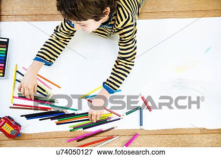 Stock Photo - Overhead view of boy lying on floor drawing on long paper. Fotosearch