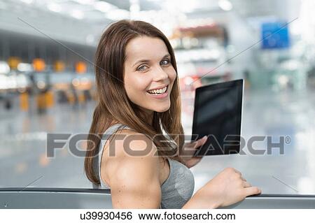 Portrait of businesswoman holding digital tablet looking over her shoulder in airport departure lounge View Large Photo Image Stock Photograph - Portrait of businesswoman holding digital tablet looking over her shoulder in airport departure lounge. Fotosearch