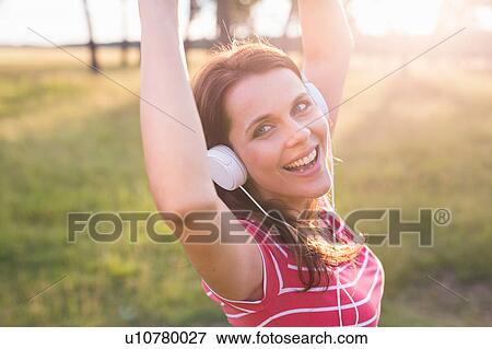 Stock Photo - Portrait of woman dancing while listening to headphone music in field. Fotosearch