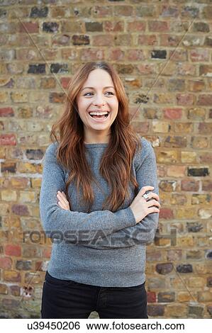 Stock Photograph - Portrait of young woman, outdoors, arms folded, laughing. Fotosearch