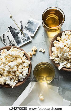 Stock Image - Still life of popcorn and drink, beside old black and white photographs, overhead view. Fotosearch