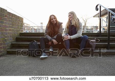 Two female friends outdoors, sitting on steps, smiling View Large Photo Image Stock Image - Two female friends outdoors, sitting on steps, smiling. Fotosearch
