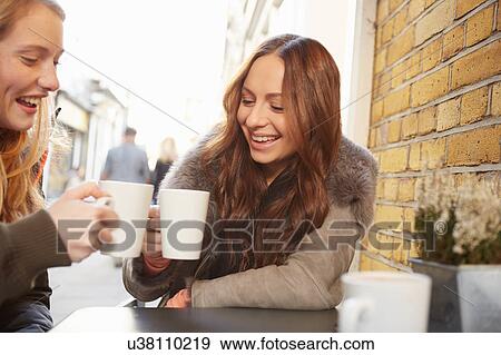 Stock Photo - Two female friends, sitting outdoors, drinking coffee, laughing. Fotosearch