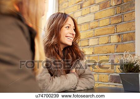 Stock Photo - Two female friends, sitting outdoors, smiling. Fotosearch